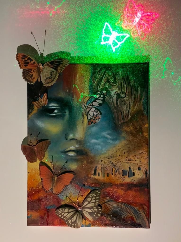 لوحة "الحلم"، امرأة حالمة تنظر إلى الجانب الأيمن، تغطيها بعض الفراشات الملونة والنصف الآخر بيوت جبلية وجذوع شجر.
